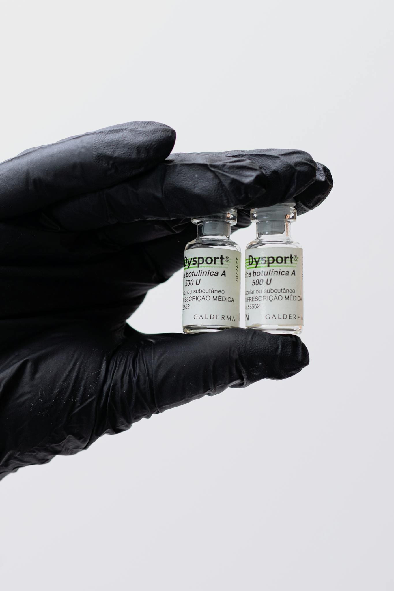 Detailed view of two botulinum toxin vials in medical gloved hand.